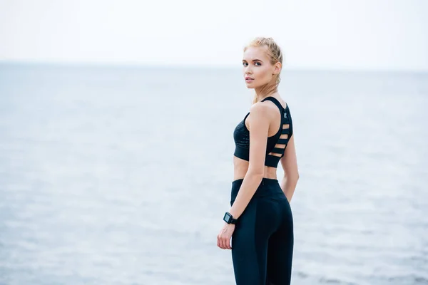Jovem loira atraente em sportswear olhando para a câmera perto do mar — Fotografia de Stock