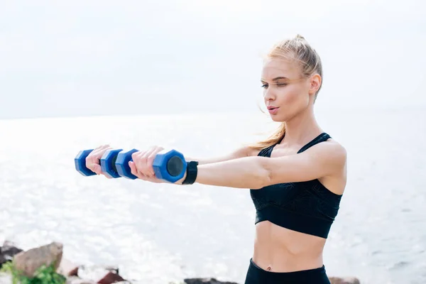 Атлетичная блондинка, тренирующаяся с гантелями у моря — стоковое фото