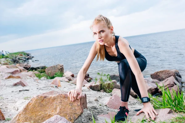 Overhead view of athletic blonde sportswoman climbing near stones and sea — Stock Photo