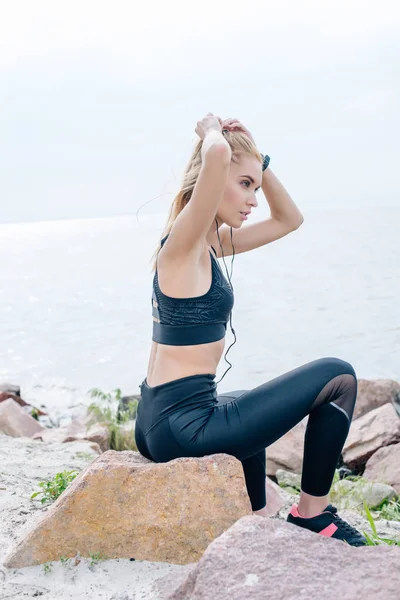 Привлекательная спортивная девушка касаясь волос во время прослушивания музыки в наушниках возле моря — стоковое фото
