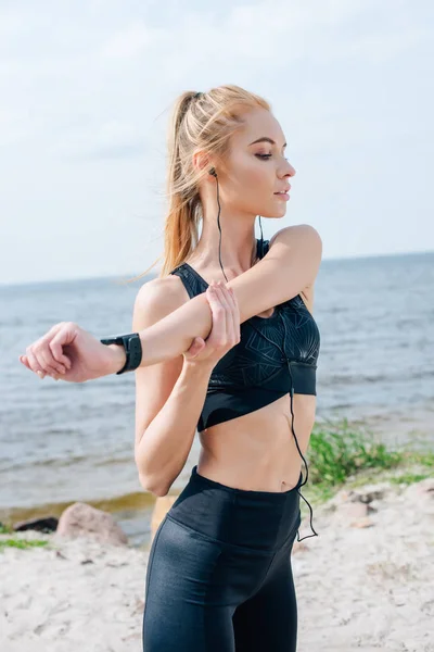 Beautiful athletic girl stretching and listening music near sea — Stock Photo