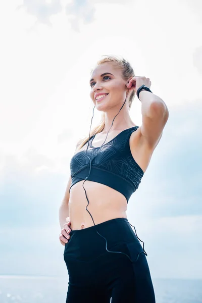 Blick auf ein fröhliches athletisches Mädchen, das Musik hört, während es mit der Hand auf der Hüfte steht — Stockfoto