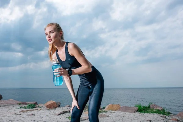 Приваблива і спортивна жінка тримає спортивну пляшку і стоїть біля моря — стокове фото