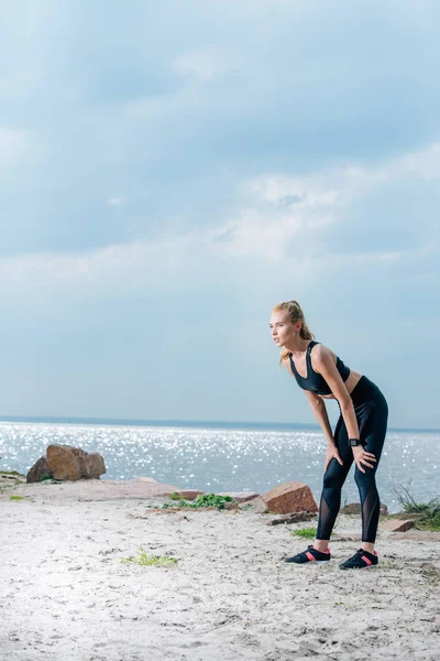 Cansado esportivo jovem mulher de pé na praia perto do mar — Fotografia de Stock