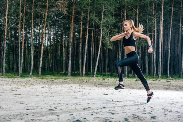 Attraktive und sportliche blonde Frau, die in der Nähe grüner Bäume läuft — Stockfoto