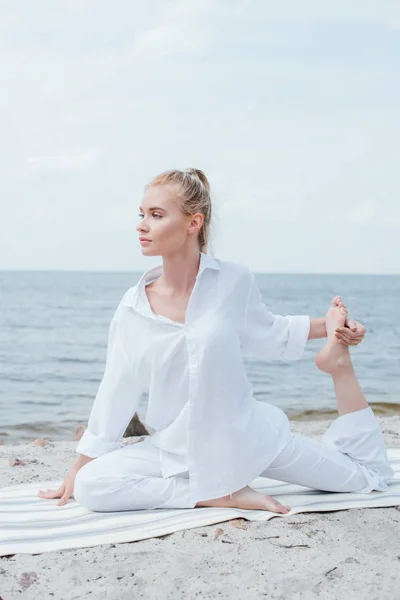 Bela mulher loira esticando no tapete de ioga perto do mar — Fotografia de Stock