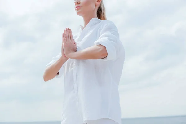 Vista recortada de la mujer de pie con las manos de oración cerca del mar - foto de stock