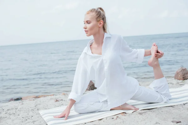 Atractiva joven rubia practicando yoga en estera de yoga cerca del mar - foto de stock