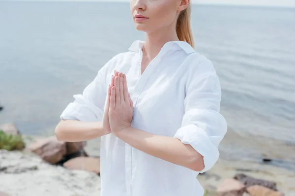 Vista recortada de la joven con las manos de oración cerca del mar - foto de stock