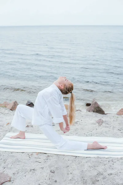 Attractive blonde  young woman doing yoga near sea — Stock Photo