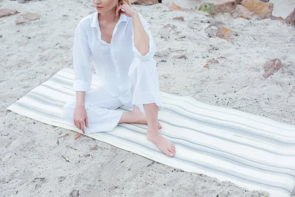 Cropped view of young woman sitting on yoga mat near sea — Stock Photo