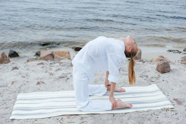 Jovem loira atraente fazendo exercício de ioga perto do mar — Fotografia de Stock