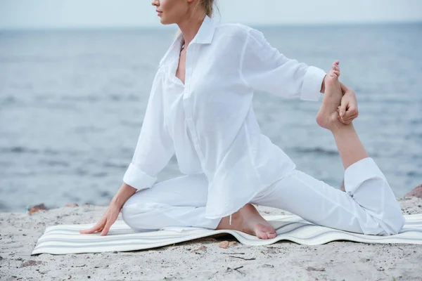 Vista recortada de una joven practicando yoga en una esterilla de yoga - foto de stock