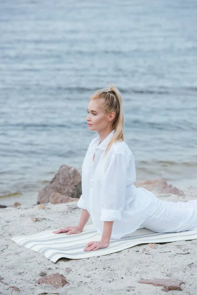 Красивая девушка практикует йогу на коврике для йоги возле реки — стоковое фото