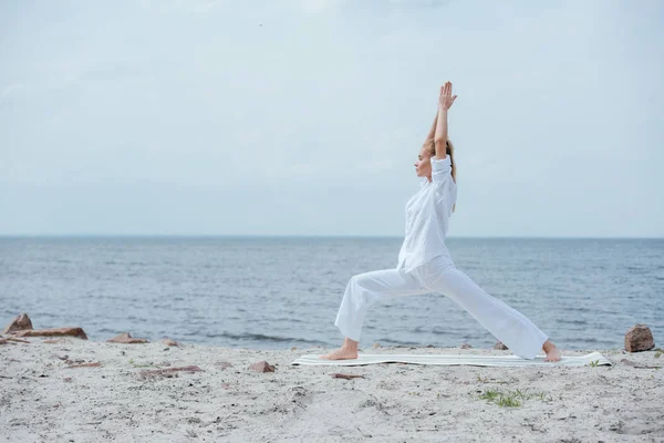 Vue latérale de la femme blonde pratiquant le yoga près de la rivière — Photo de stock
