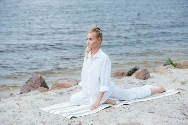 Attractive blonde young woman practicing yoga near river on yoga mat — Stock Photo