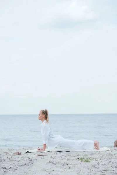 Side view of young woman practicing yoga near river — Stock Photo