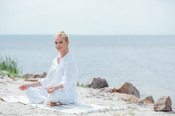 Happy blonde woman practicing yoga near sea — Stock Photo