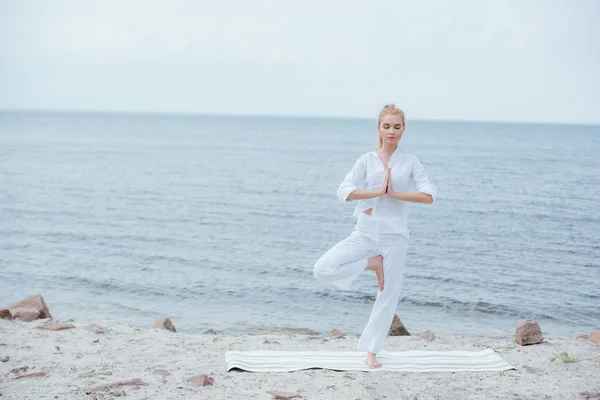 Femme blonde avec les yeux fermés pratiquant le yoga sur tapis de yoga — Photo de stock