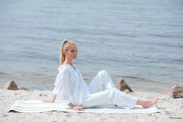 Attraente donna bionda con gli occhi chiusi seduta su tappetino yoga — Foto stock