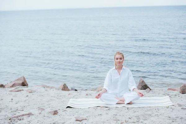 Friedliche und schöne blonde junge Frau praktiziert Yoga in der Nähe des Flusses — Stockfoto