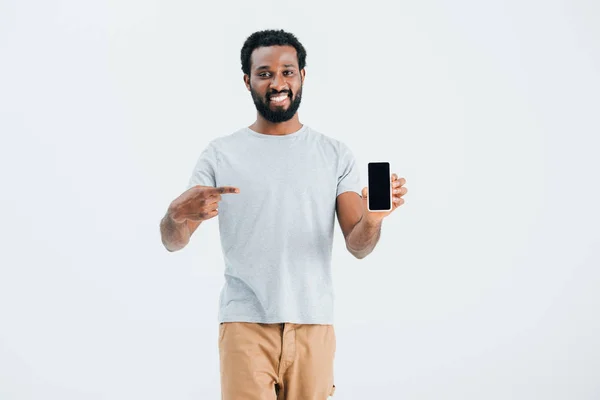 Homme afro-américain souriant pointant vers le smartphone, isolé sur gris — Photo de stock