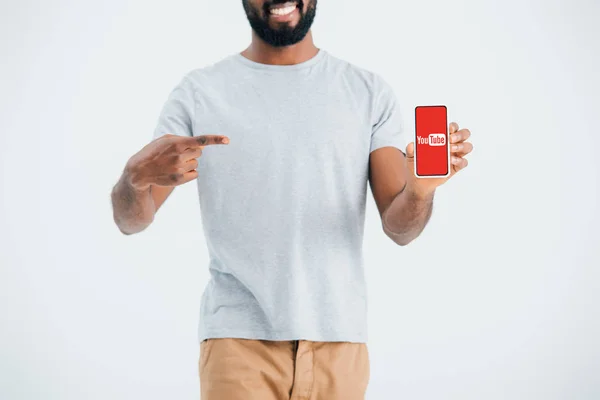 KYIV, UKRAINE - MAY 17, 2019: cropped view of african american man pointing at smartphone with youtube app, isolated on grey — Stock Photo