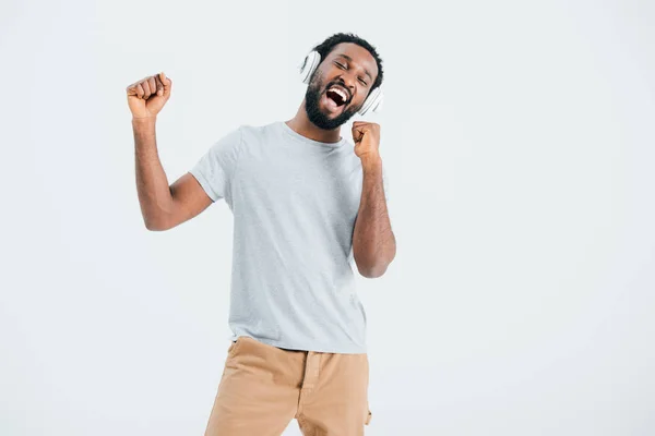 Збуджений афроамериканський чоловік співає і слухає музику з навушниками, ізольований на сірому — стокове фото