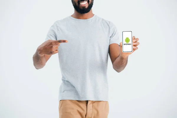 KYIV, UKRAINE - MAY 17, 2019: cropped view of african american man pointing at smartphone with android app, isolated on grey — Stock Photo