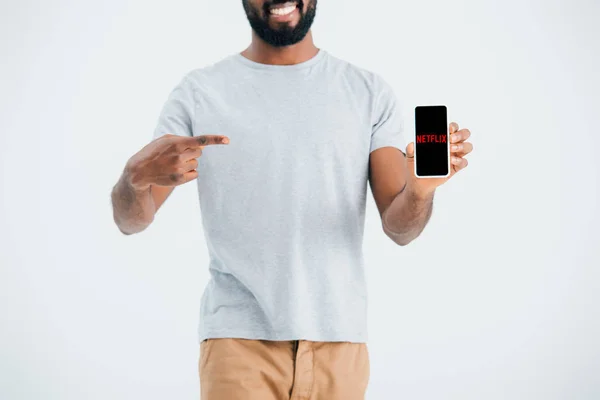 KYIV, UCRAINA - 17 MAGGIO 2019: vista ritagliata dell'uomo afroamericano che punta lo smartphone con l'app netflix, isolato su grigio — Foto stock