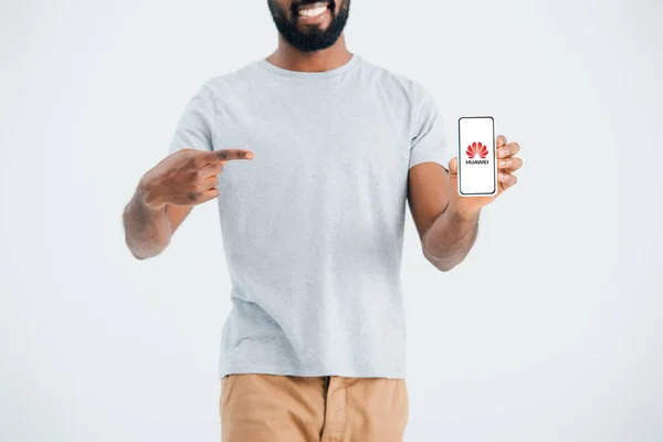 KYIV, UCRANIA - 17 DE MAYO DE 2019: vista recortada del hombre afroamericano apuntando a un teléfono inteligente con hue.net app, aislado en gris - foto de stock