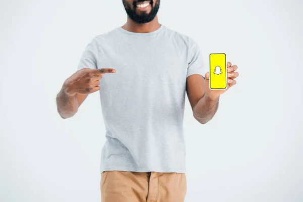 KYIV, UKRAINE - 17 MAI 2019 : vue recadrée d'un homme afro-américain pointant vers un smartphone avec l'application Snapchat, isolé sur gris — Photo de stock