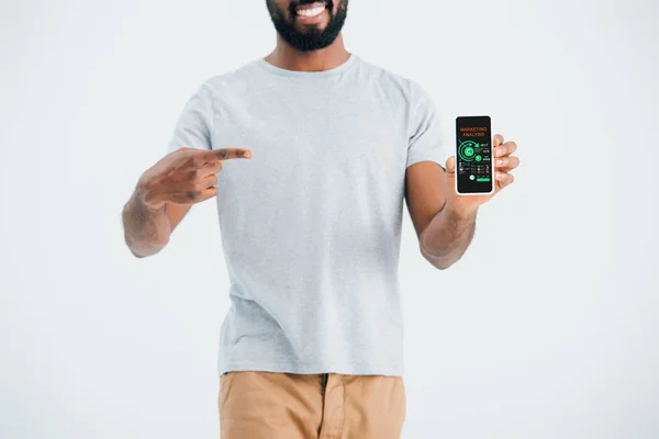 Обрезанный вид африканского американца, указывающего на смартфон с помощью приложения маркетингового анализа, изолированного на сером — стоковое фото