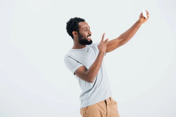 Hombre afroamericano con signo de victoria tomando selfie en el teléfono inteligente, aislado en gris - foto de stock