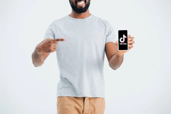 KYIV, UKRAINE - 17 MAI 2019 : vue recadrée d'un homme afro-américain pointant du doigt un smartphone avec l'application Tik Tok, isolé sur gris — Photo de stock