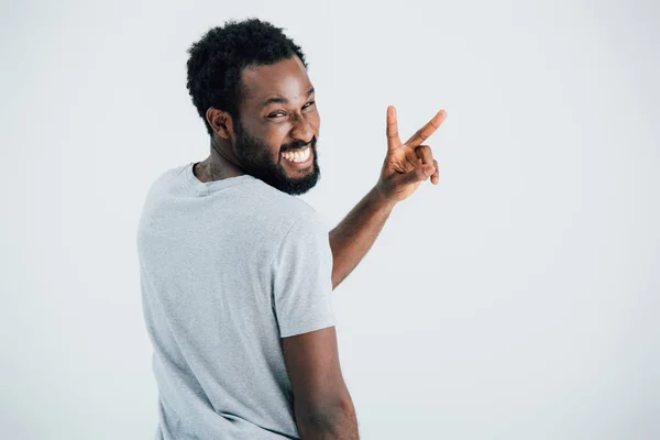 Glücklicher afrikanisch-amerikanischer Mann in grauem T-Shirt mit Siegeszeichen isoliert auf grau — Stockfoto