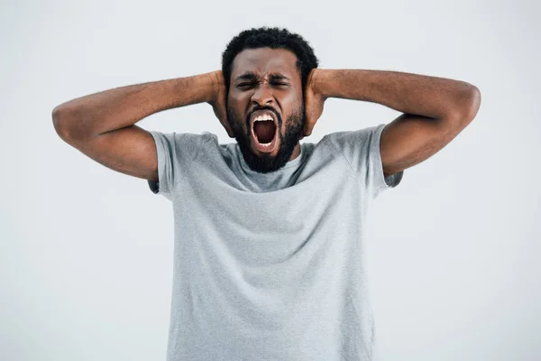 Emotionale afrikanisch-amerikanische Mann in grauem T-Shirt schreit und schließt Ohren isoliert auf grau — Stockfoto