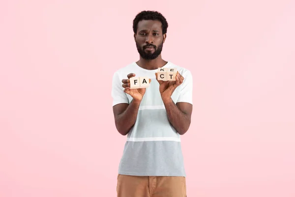 African american man holding alphabet cubes with fact word, isolated on pink — Stock Photo