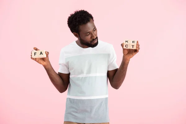 Hombre afroamericano mirando cubos de alfabeto con palabra de hecho, aislado en rosa - foto de stock