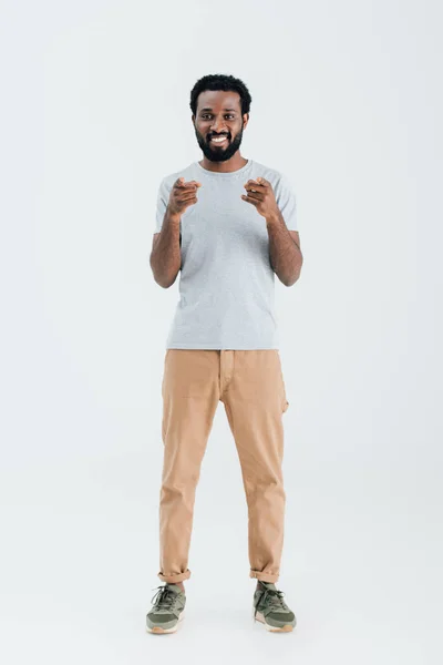 Lächelnder afrikanisch-amerikanischer Mann in grauem T-Shirt zeigt vereinzelt auf grau — Stockfoto