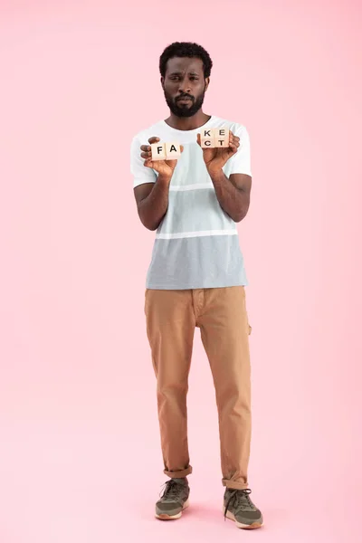 Bonito afro-americano homem segurando cubos alfabeto com palavra fato, isolado em rosa — Fotografia de Stock