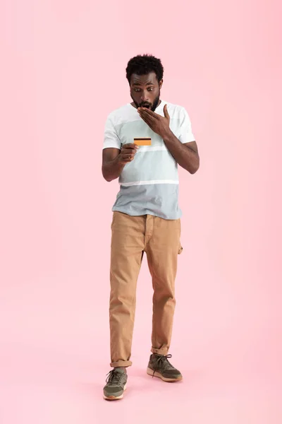 Здивований афроамериканський чоловік показує кредитну картку ізольовано на рожевому — стокове фото