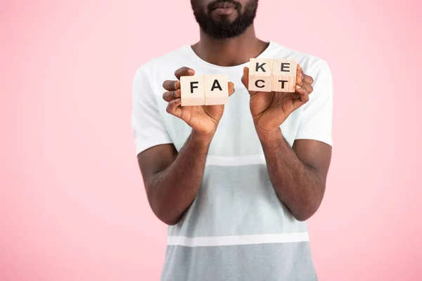 Vista cortada do homem americano africano segurando cubos alfabeto com palavra fato, isolado em rosa — Fotografia de Stock
