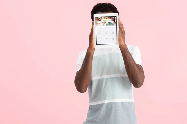 KYIV, UCRANIA - 17 DE MAYO DE 2019: hombre afroamericano gritando y mostrando tableta digital con aplicación cuadrada, aislado en rosa — Stock Photo