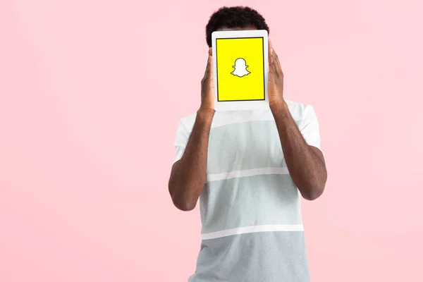 КИЕВ, Украина - 17 мая 2019 года: Африканский американец кричит и показывает цифровой планшет с приложением Snapchat, изолированный на розовом — стоковое фото