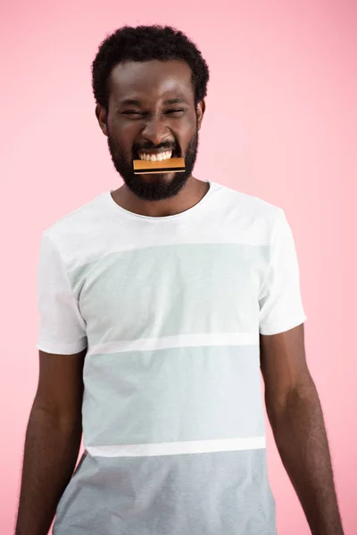 Cheerful african american man biting credit card isolated on pink — Stock Photo