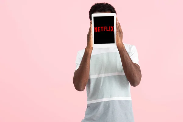 KYIV, UCRANIA - 17 DE MAYO DE 2019: hombre afroamericano gritando y mostrando tableta digital con aplicación netflix, aislado en rosa - foto de stock