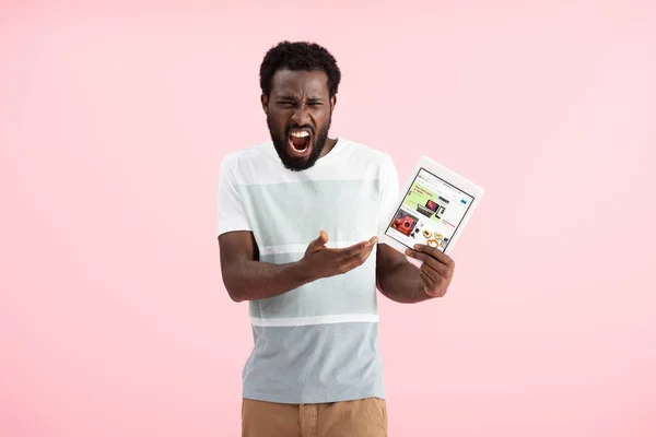 KYIV, UKRAINE - MAY 17, 2019: emotional african american man shouting and showing digital tablet with ebay app, isolated on pink — Stock Photo