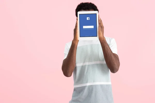 KYIV, UCRANIA - 17 DE MAYO DE 2019: hombre afroamericano gritando y mostrando tableta digital con aplicación de facebook, aislado en rosa — Stock Photo