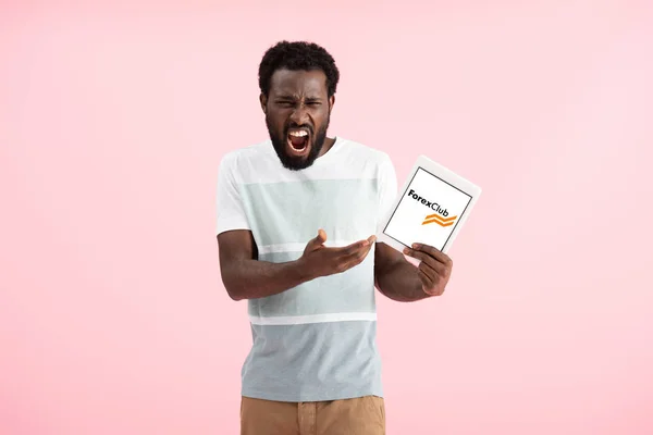 KYIV, UKRAINE - MAY 17, 2019: emotional african american man shouting and showing digital tablet with forex club app, isolated on pink — Stock Photo